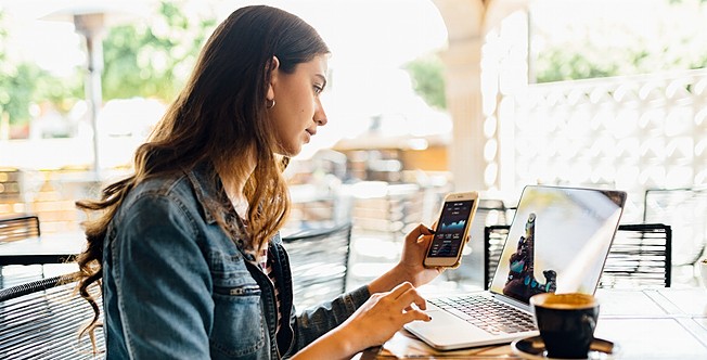 Woman using data on laptop and mobile phone while sitting in cafe